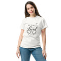 White He First Loved Us Christian T-shirt featuring 1 John 4:19 cross and botanical design