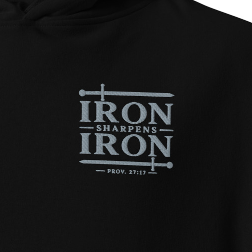 Close-up of black Iron Sharpens Iron Proverbs 27:17 premium embroidered Christian hoodie with silver sword chest embroidery.
