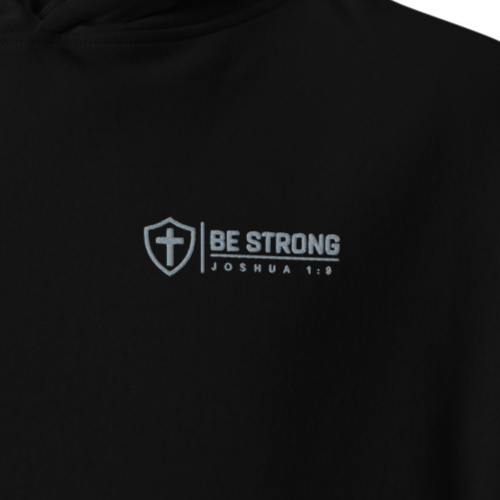 Close-up of black Be Strong Joshua 1:9 premium embroidered Christian hoodie with silver cross and shield chest embroidery.
