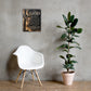 A framed wall art print with a Bible verse hangs on a textured gray concrete wall above a white molded chair and next to a potted fiddle-leaf fig plant.