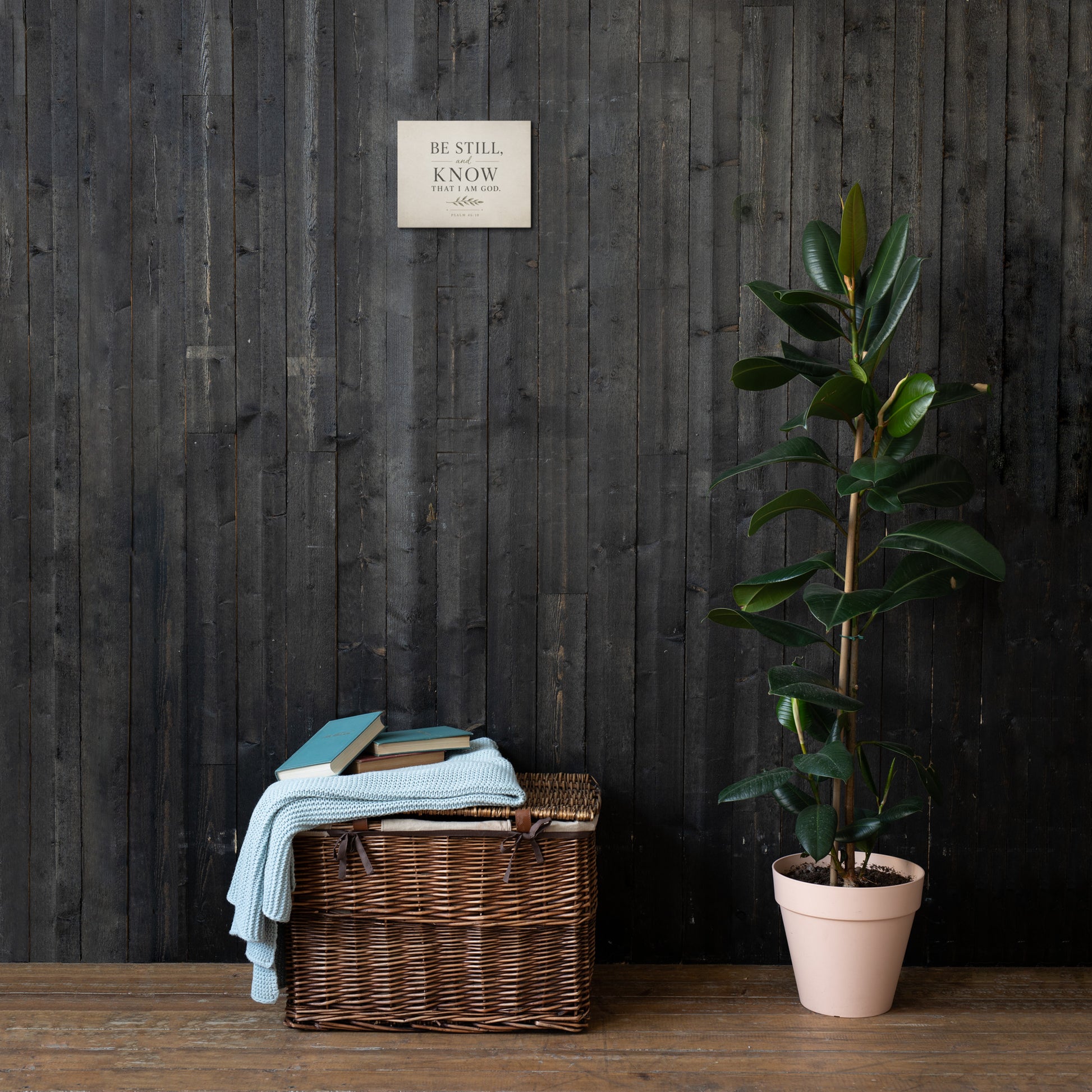 Be Still and Know Christian Scripture canvas displayed on dark wood wall above basket and plant